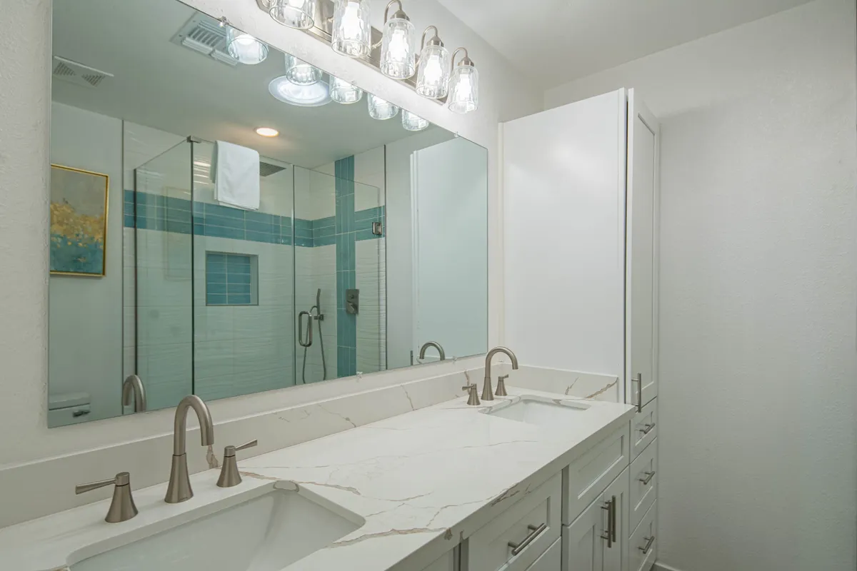 A modern bathroom featuring a double sink vanity, large mirrors, a glass shower enclosure, and subtle wall art. Bright and spacious, it exudes an invigorating yet restful feel ideal for self-care routines.