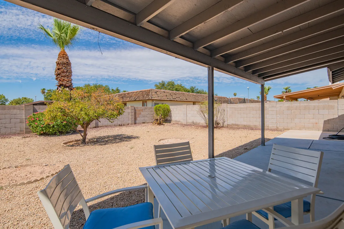 An inviting exterior featuring a patio table under a palm tree in a landscaped garden, with the home’s structure visible in the background. The scene highlights opportunities for outdoor dining or relaxation amid greenery, suggesting an ideal spot for unwinding after pet adventures.