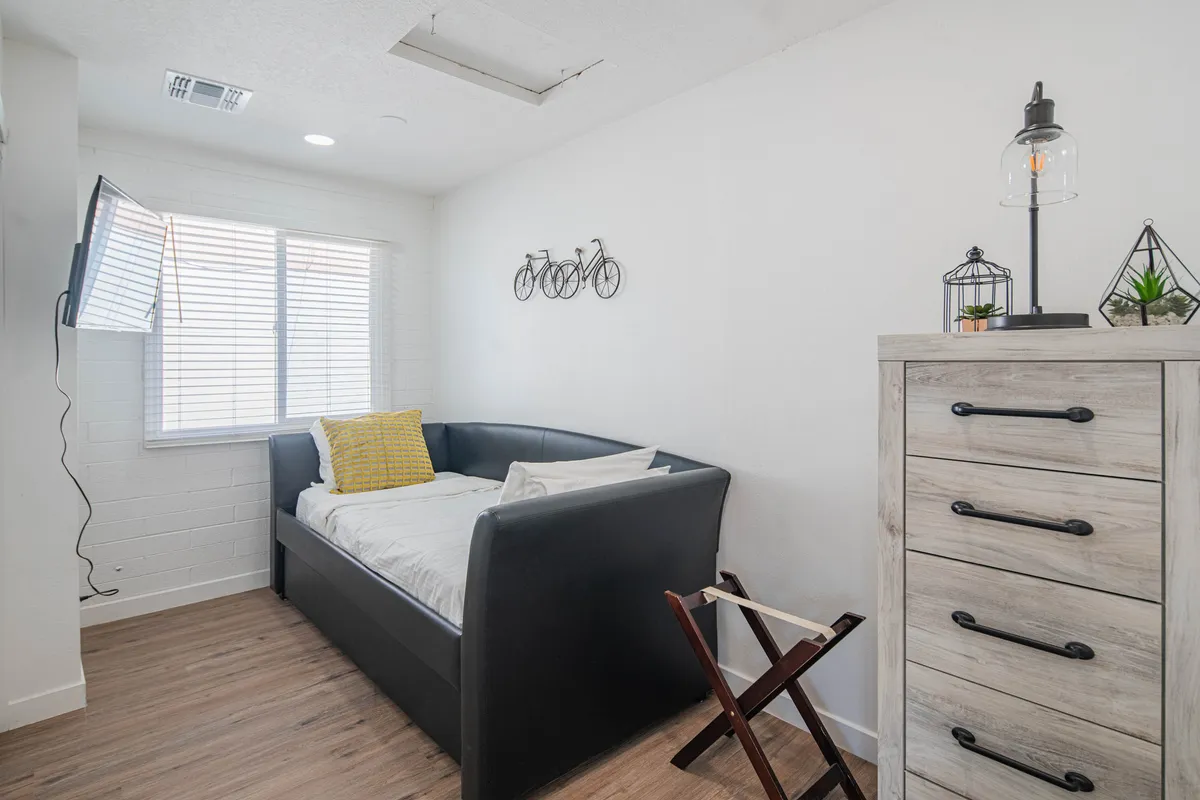 A welcoming bedroom with a bed, bicycle-themed wall art, lamp, and dresser. The soft lighting and inviting setup suggest a cozy space for reading, relaxing, or setting up a home office.